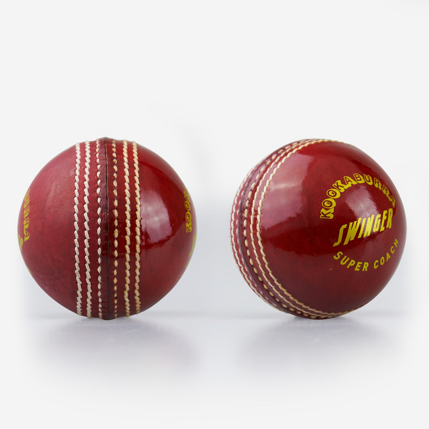 Two shiny red Kookaburra Super Coach Swinger leather cricket balls with white stitching—one shows the seam, while the other displays Kookaburra branding—ideal for swing training on a plain white background.