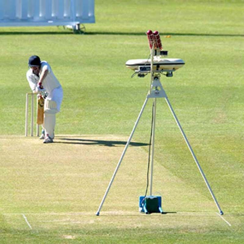 A cricket player ready to bat stands on the pitch, while a set of 3 Bola Short Legs by Bola are positioned nearby on the field—perfect for junior cricket practice sessions.