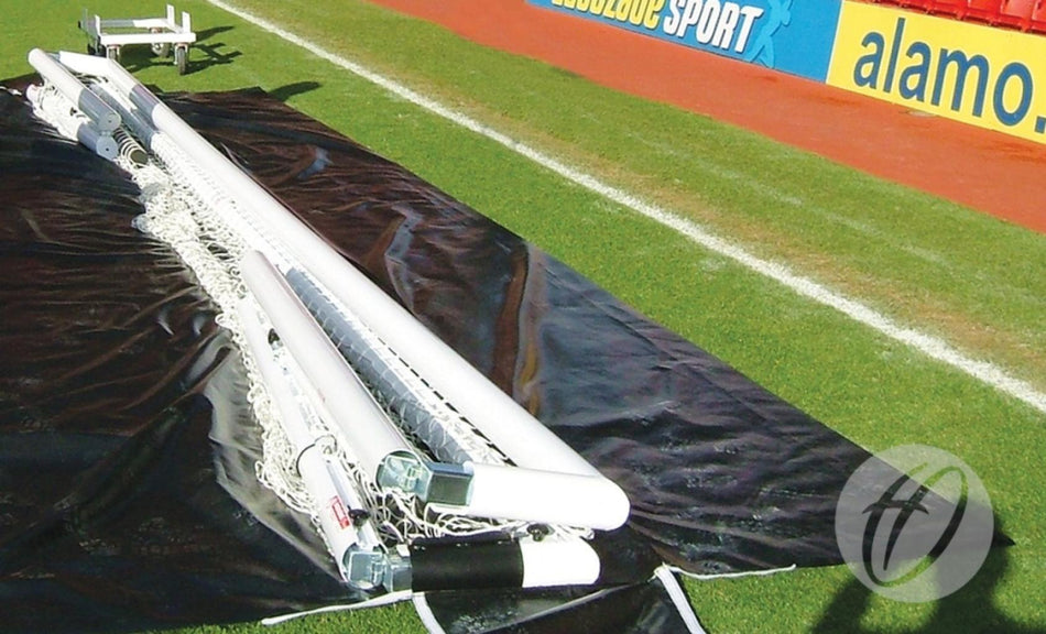 Disassembled soccer goalposts and nets, including a Harrod Sport 3G Foldaway Euro Portagoal, are laid out on a black tarp over green grass beside a red running track and advertising boards at a sports stadium, with a Harrod Sport Spare 3G Stadium Foldaway Goal Bag nearby.