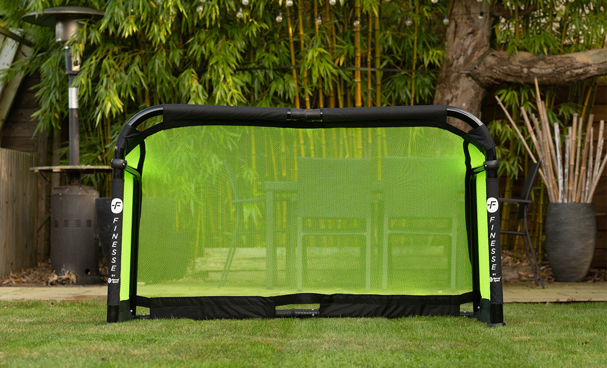 The Finesse Folding Target Goal by FINESSE is set up on a grassy lawn, with patio furniture and bamboo plants behind—ideal for fast assembly and outdoor games.