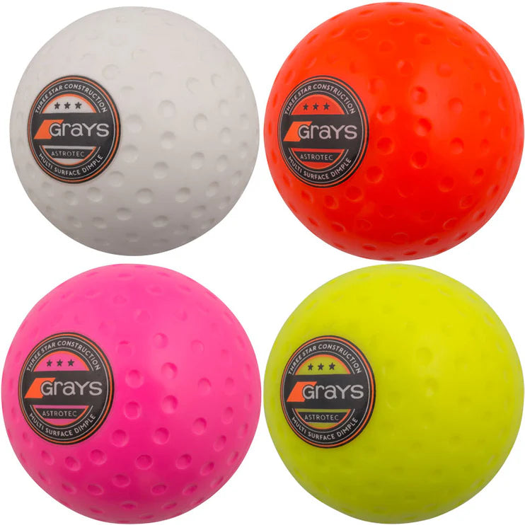 Four Grays Astrotec Hockey Balls in white, orange, pink, and yellow—each with a circular Grays logo—are shown against a plain background. Ideal for club matches at county level.