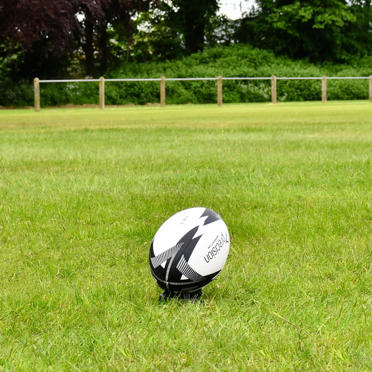 Black and grey Precision Momentum Rugby Training Ball placed on a kicking tee on grass