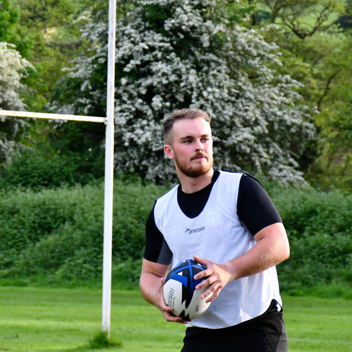 Player in a white training bib holding the blue Precision Momentum Rugby Training Ball ready to pass