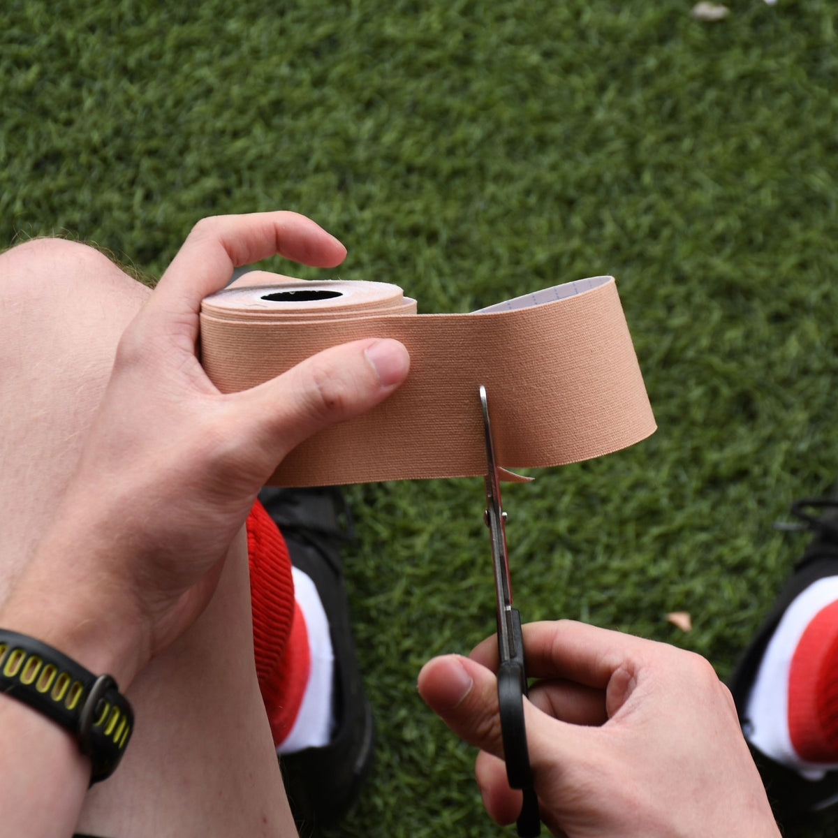 Cutting a strip of beige Precision kinesiology tape from the roll with scissors