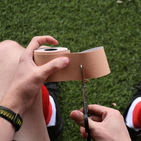Cutting a strip of beige Precision kinesiology tape from the roll with scissors