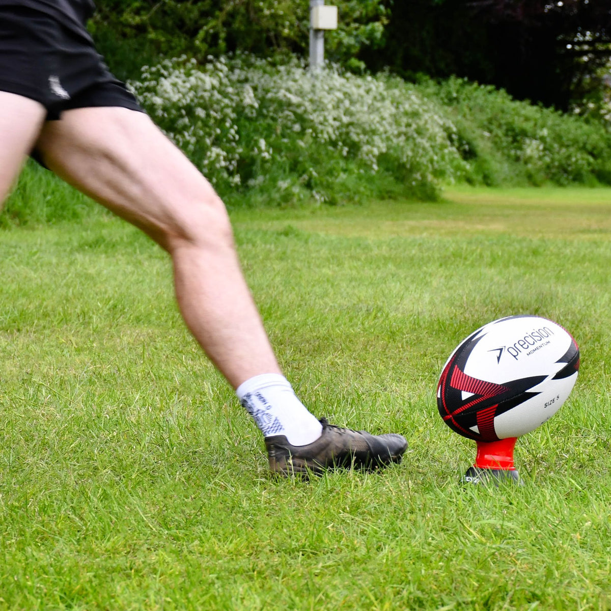Player's leg swinging toward the red Precision Momentum Rugby Training Ball on a kicking tee