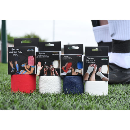 Precision cohesive tape retail boxes with red, white and navy rolls on grass beside players