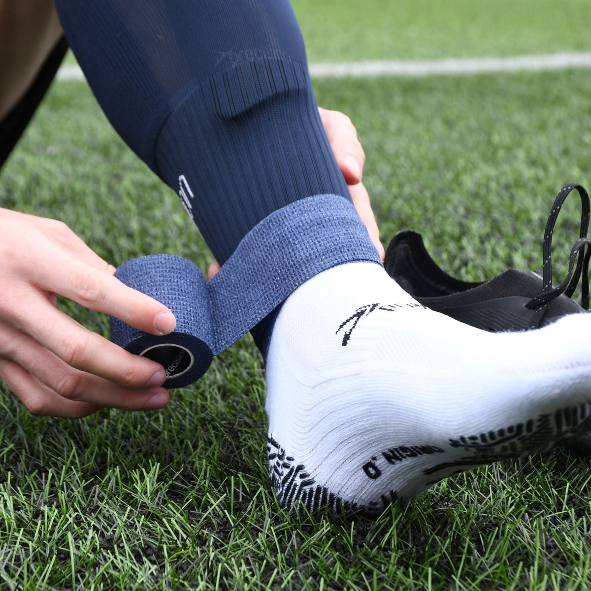 Player wrapping navy Precision cohesive tape around a navy football sock above a white grip sock