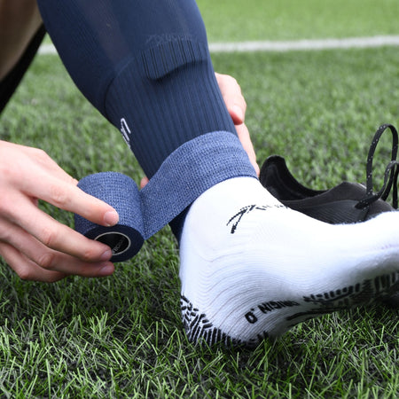 Player wrapping navy Precision cohesive tape around a navy football sock above a white grip sock