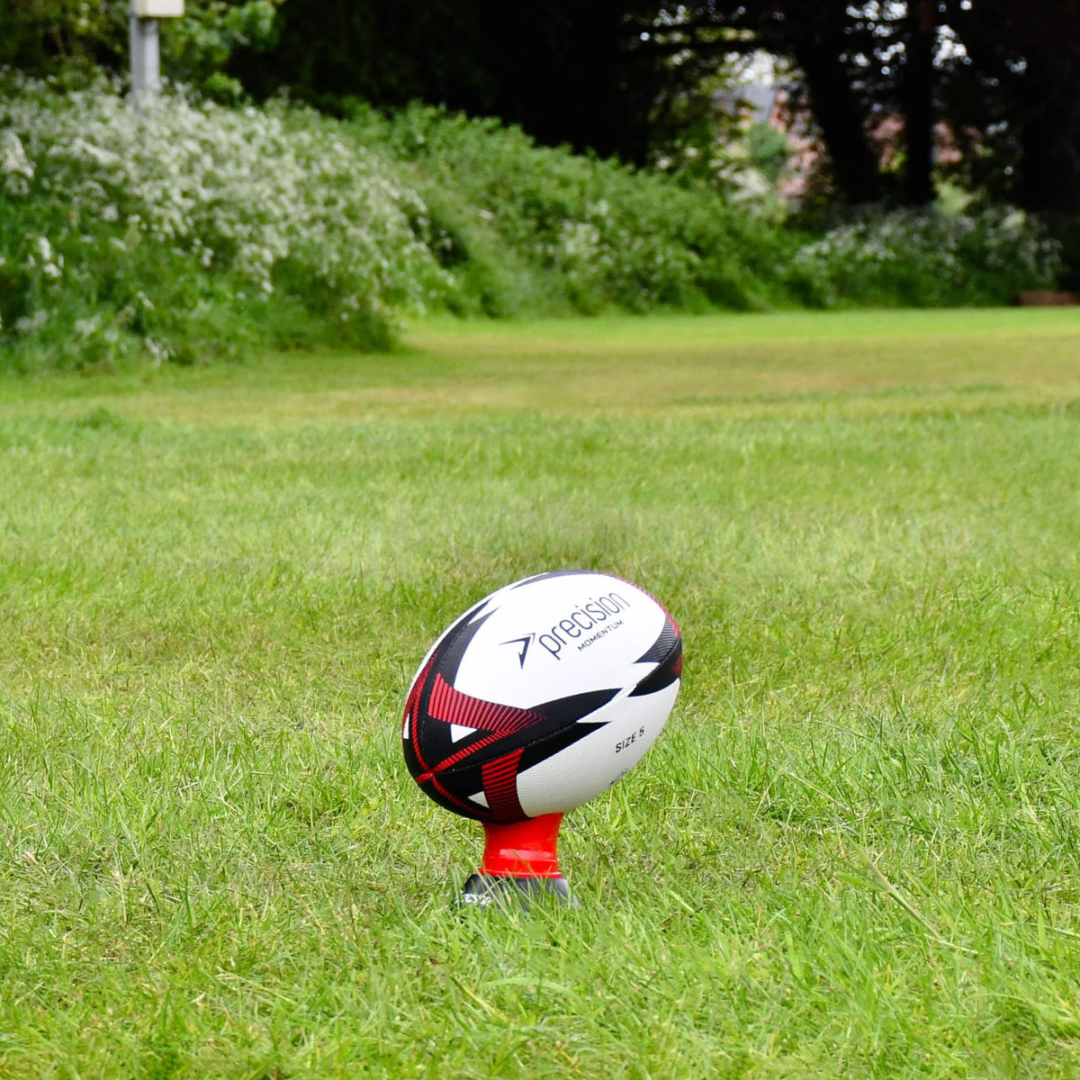 Red Precision Momentum Rugby Training Ball standing on a red kicking tee on grass