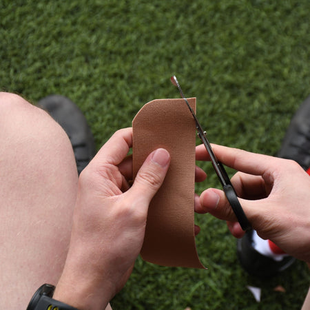 Rounding the corners of a beige Precision kinesiology tape strip with scissors
