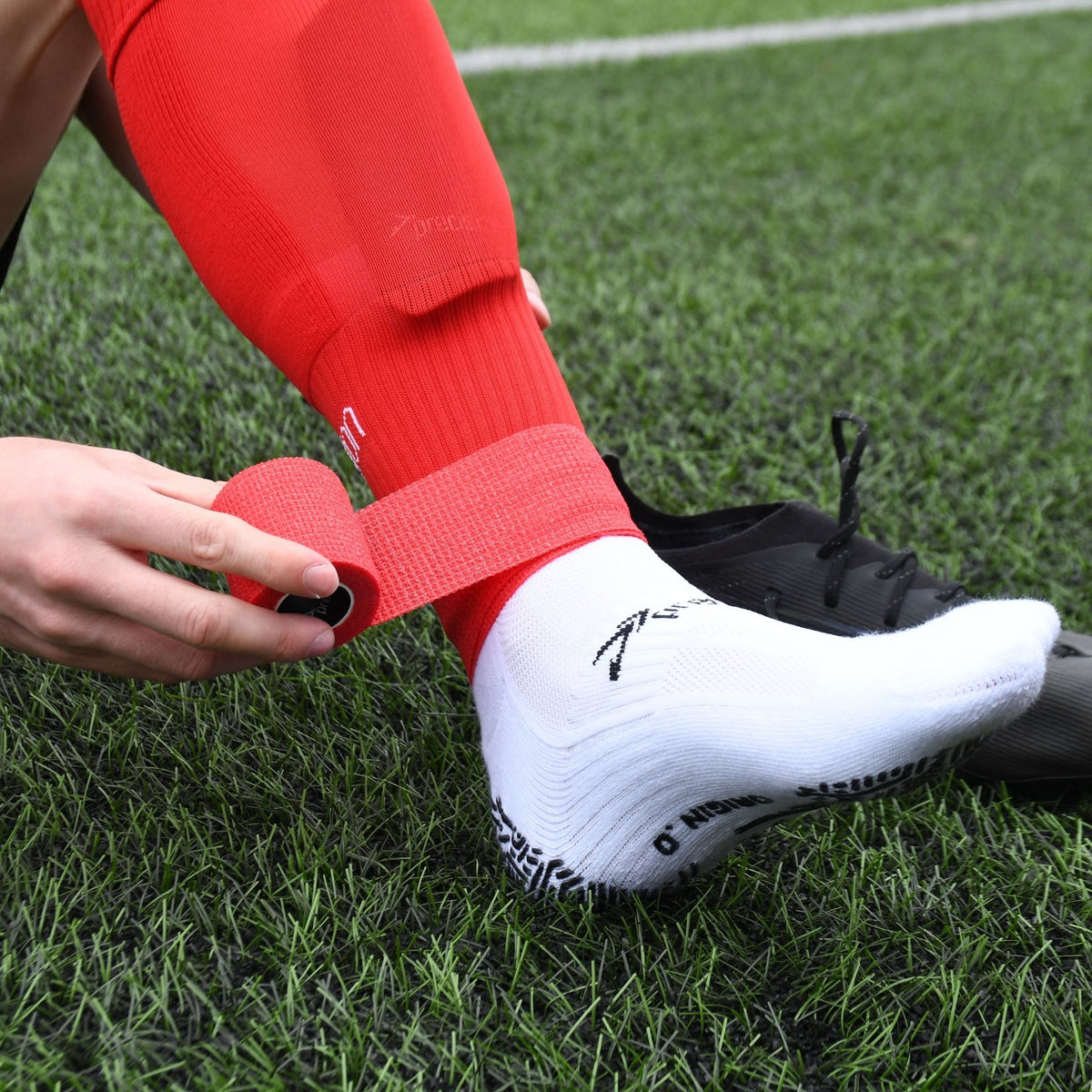 Player wrapping red Precision cohesive tape around a red football sock on the pitch