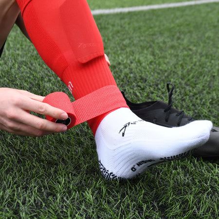 Player wrapping red Precision cohesive tape around a red football sock on the pitch