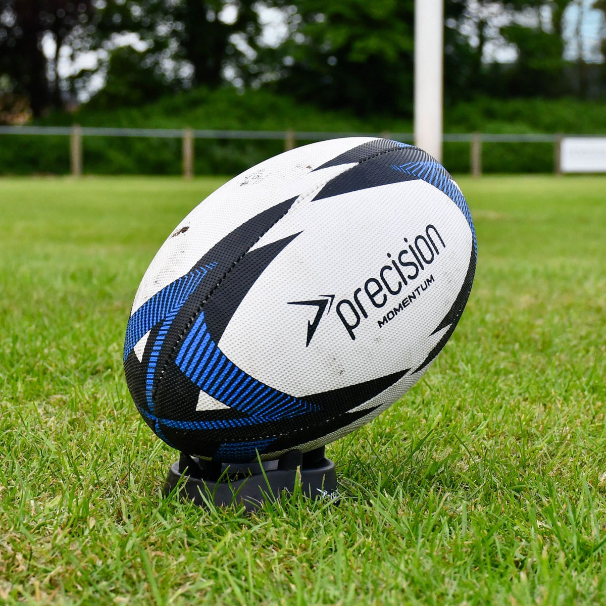 Blue Precision Momentum Rugby Training Ball resting on a kicking tee on a grass pitch