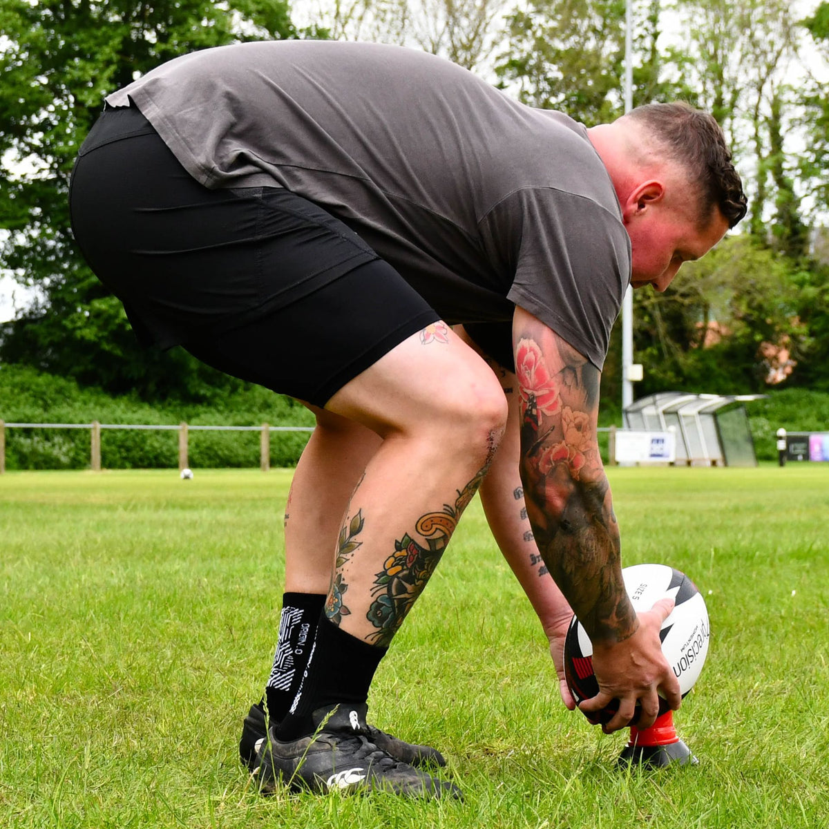 Player bending to set the red Precision Momentum Rugby Training Ball on a tee before a kick