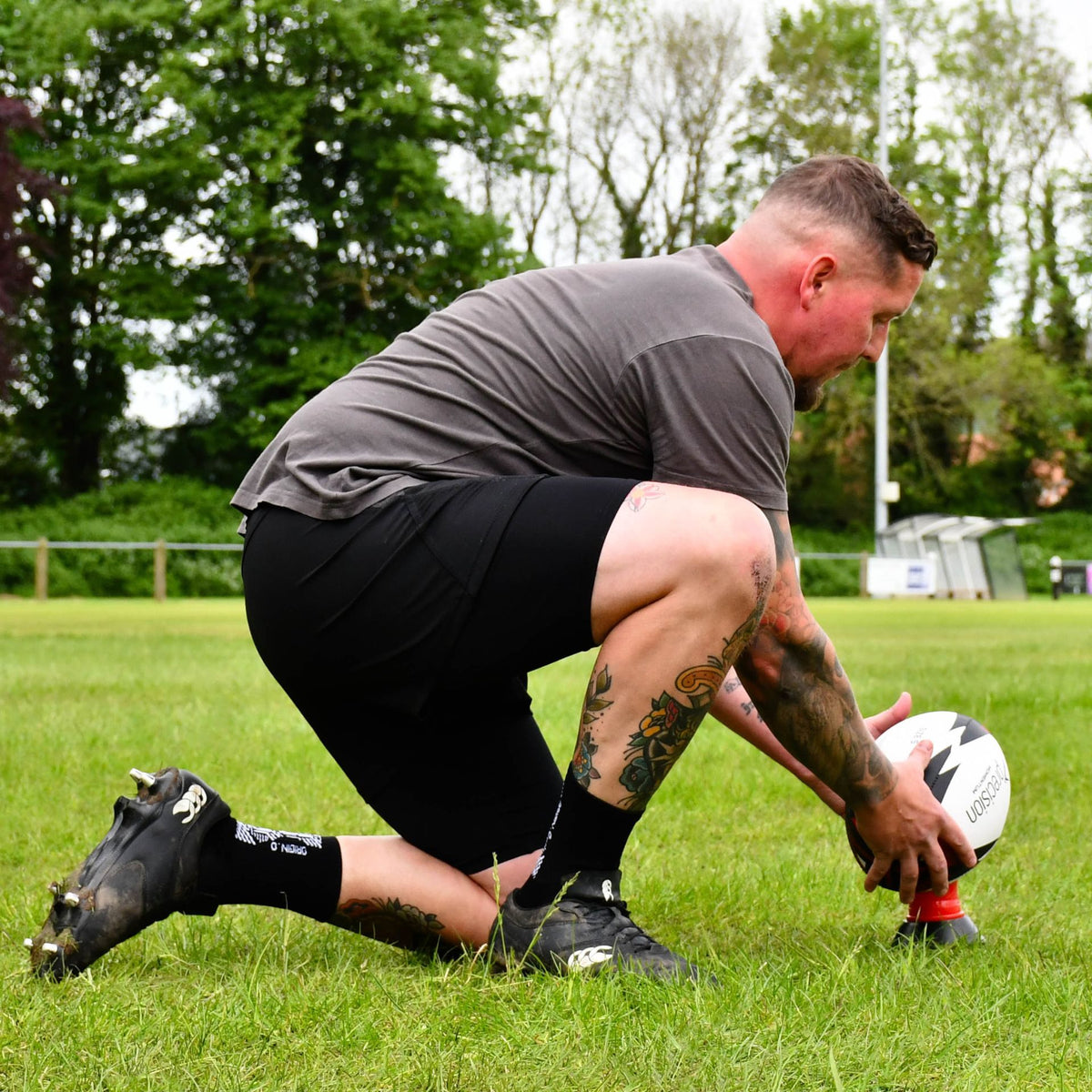 Player kneeling to place the red Precision Momentum Rugby Training Ball on a kicking tee