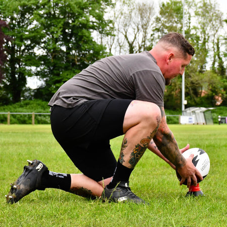 Player kneeling to place the red Precision Momentum Rugby Training Ball on a kicking tee