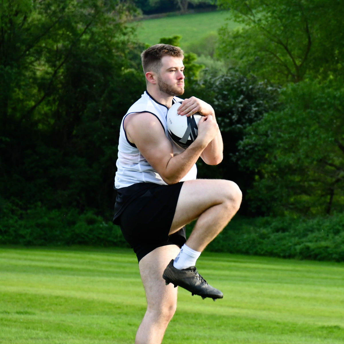 Player in a white bib raising his knee while holding the Precision Momentum Rugby Training Ball