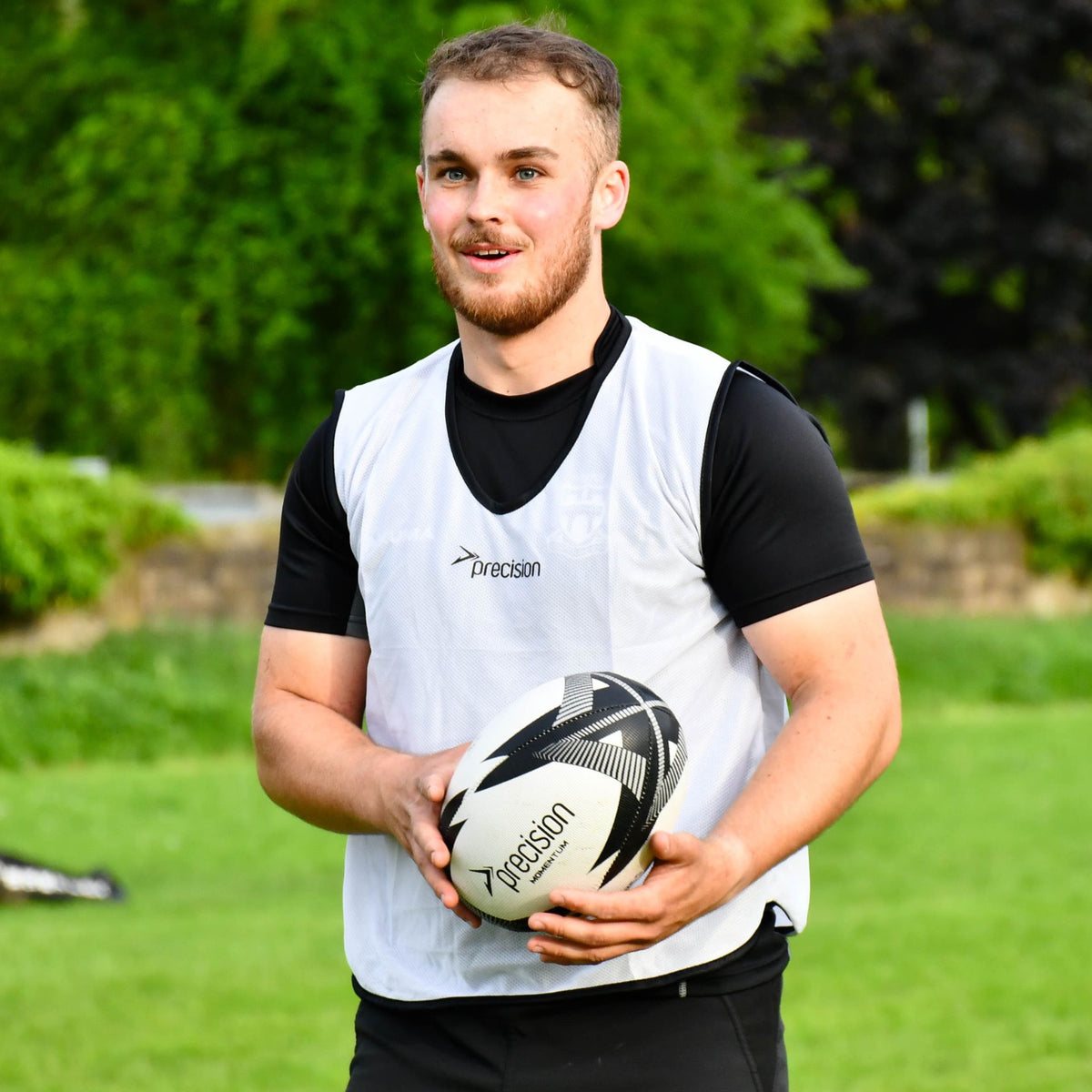 Smiling player in a white bib holding the grey Precision Momentum Rugby Training Ball