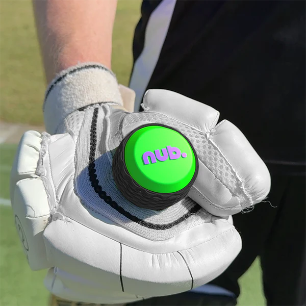 A person wearing a white cricket glove holds the nub - Green Thunder by nub Sports, a popular silicone cricket bat grip with a bright green top and purple "nub." lettering. The background features a grassy outdoor area.