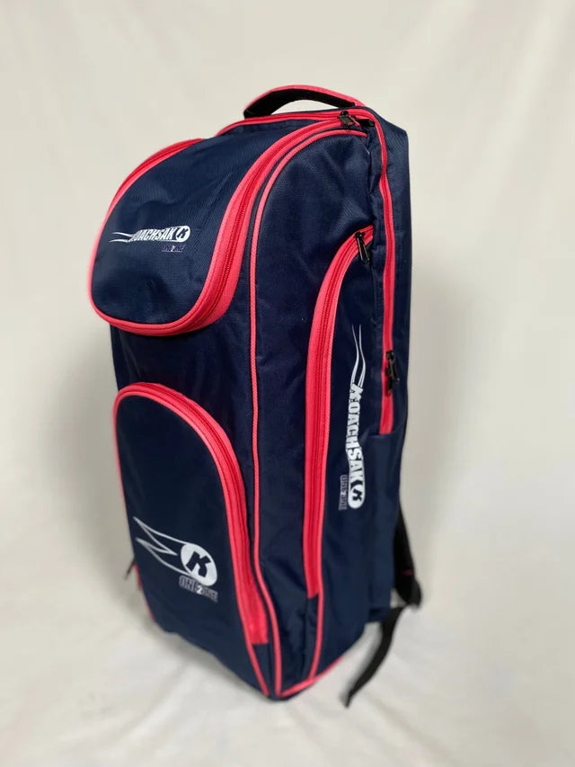 The Katchet KoachSak One2One bag in navy and pink, featuring the brand logo on the side and top, stands upright against a plain light background—ideal for carrying cricket equipment or one-to-one coaching sessions.