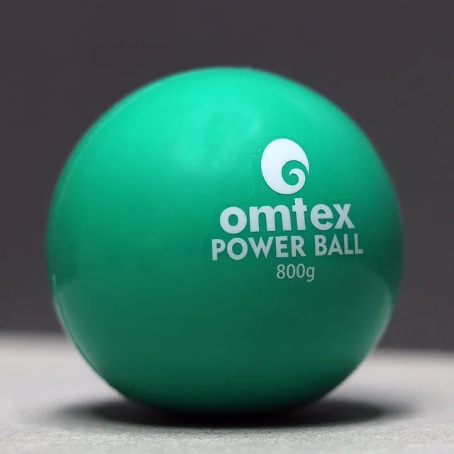 An Omtex PowerBall, a green weighted cricket ball by Omtex for training and boosting batting power, is placed on a light surface against a dark background.