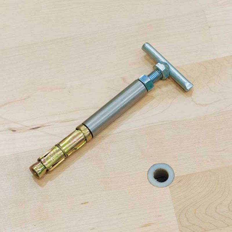 A Harrod Sport SH2 Sports hall Floor Plug, 160MM, rests on a wooden surface beside a drilled hole—engineered for secure and precise anchoring in specialist flooring systems, much like how a metal dowel jig tool ensures accurate alignment and installation in woodworking projects.