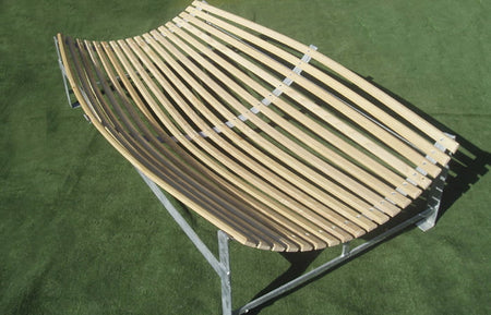 The Martin Berrill Sports Wooden Slip Catch Cradle features a modern curved seat with evenly spaced hardwood ash slats and a metal frame, designed for outdoor use on grassy surfaces.