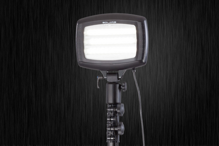 The Nightsearcher SportStar Portable LED Floodlight, delivering 20,000 lumens, is mounted on a black tripod stand with a power cable attached and shines brightly against a dark, textured background.