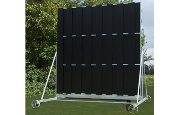 The Martin Berrill Sports Twenty/20 Sight Screen is a large, freestanding black screen with vertical panels and a high-visibility backdrop, mounted on a white metal frame, shown outdoors with grass and trees in the background.