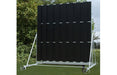 The Martin Berrill Sports Twenty/20 Sight Screen is a large, freestanding black screen with vertical panels and a high-visibility backdrop, mounted on a white metal frame, shown outdoors with grass and trees in the background.