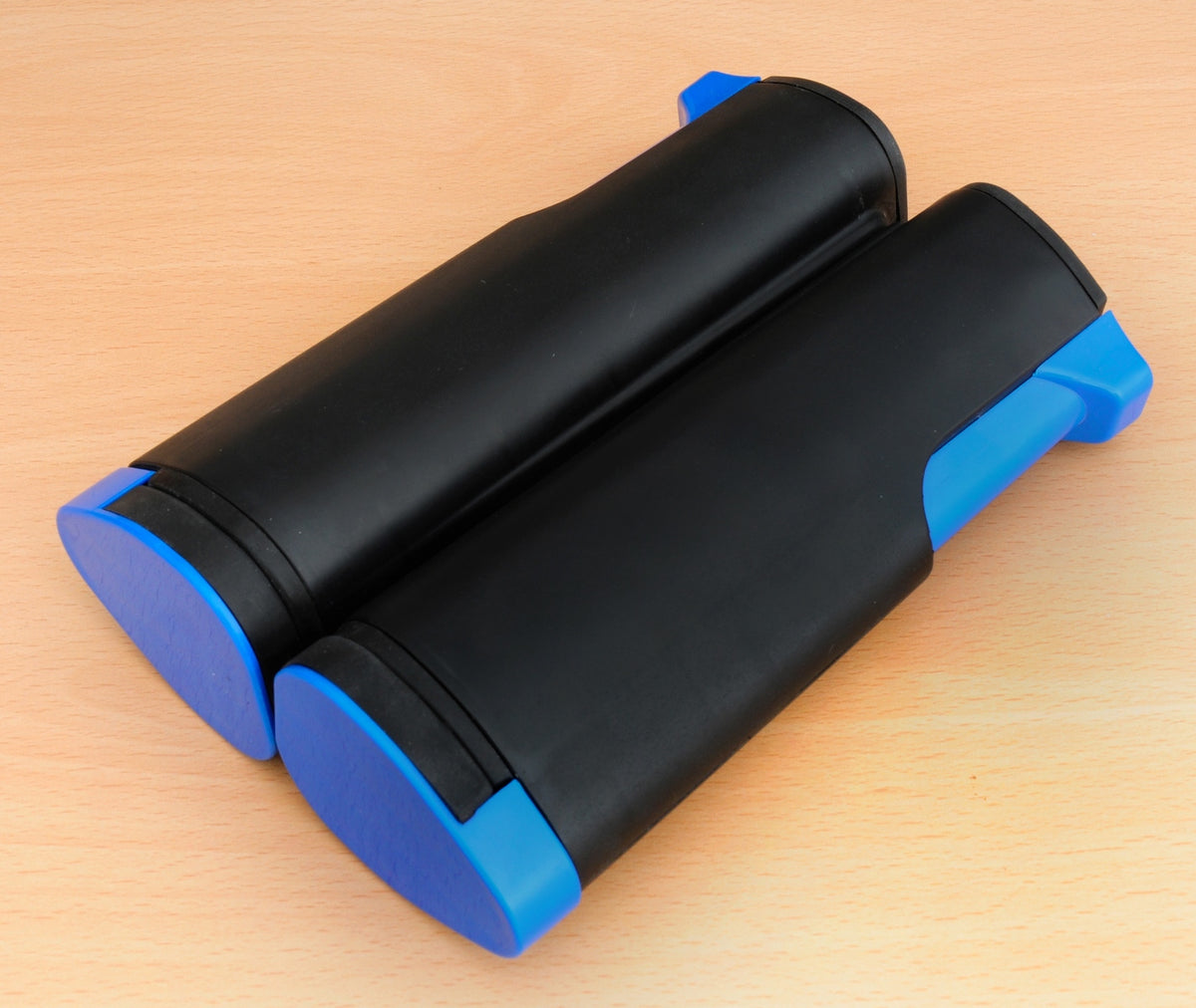 Two black and blue toner cartridges, with blue caps on one end, are placed side by side on a light wooden surface. Their sleek design is reminiscent of the Sure Shot Matthew Syed Flex Net by Sure Shot.