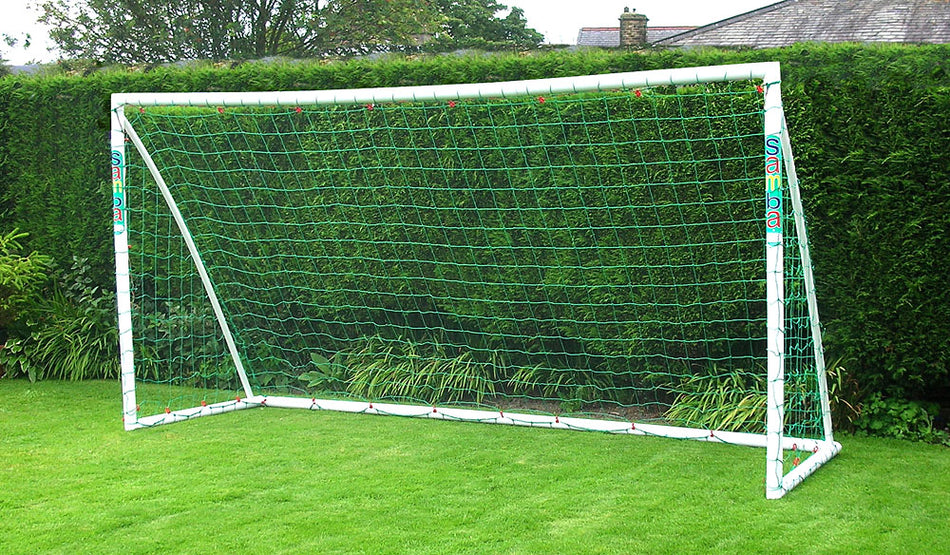 The Samba Trainer Goal 12 x 6 by Samba Sports, featuring a white uPVC frame and green net, is set on a pristine grassy lawn bordered by tidy hedges—an ideal garden football goal for family fun.