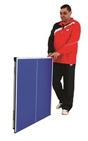A man in a red and black jacket stands beside a folded Butterfly Starter Table Tennis Table by Butterfly, showcasing its space-saving, upright storage.