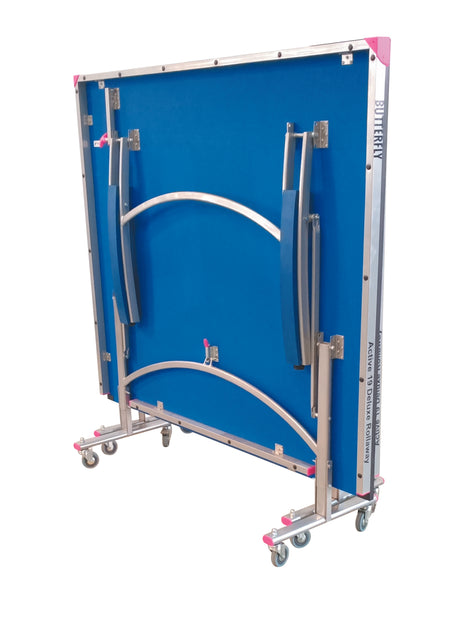 The Butterfly Active 19 Deluxe Rollaway Table Tennis Table by Butterfly features a 19mm blue playing top, metal frame with wheels, and pink corner protectors, folded upright for easy storage or transport.