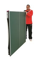 A person in a red jacket stands behind and holds a folded Butterfly Europa 25 Table Tennis Table by Butterfly, set on its side.