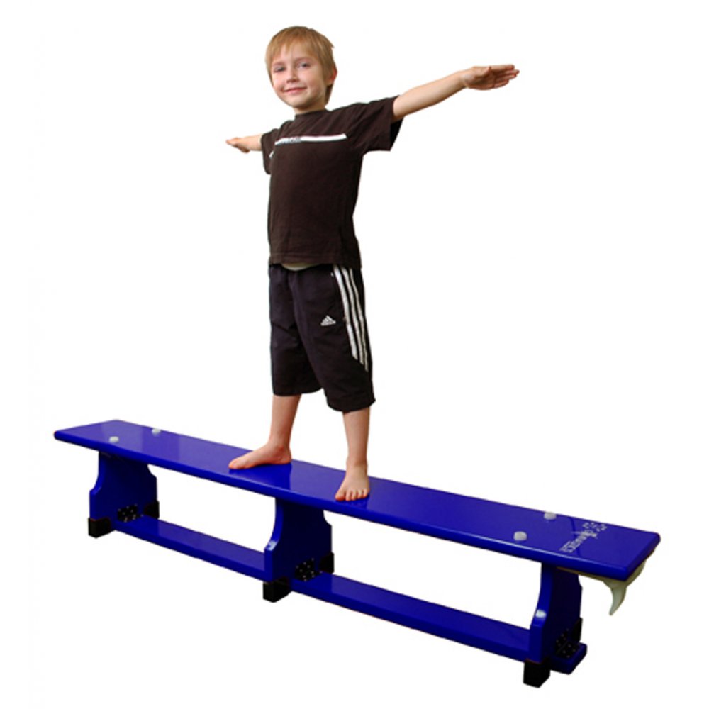 A young boy balances barefoot with arms outstretched, smiling, on a blue Sure Shot Coloured Balance Bench (6ft) by Sure Shot. He wears a black t-shirt and black shorts with white stripes.