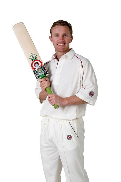 A man wearing a Hunts County Active Cricket Shirt 3/4 Sleeve, Activ Fit, holds a cricket bat and smiles at the camera against a plain white background.
