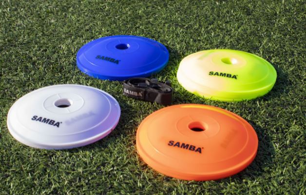 The Samba Sports Samba Flat Marker set includes four colored cones (blue, yellow, white, orange) on green turf with a black strap—ideal coaching markers for drills and practice sessions.