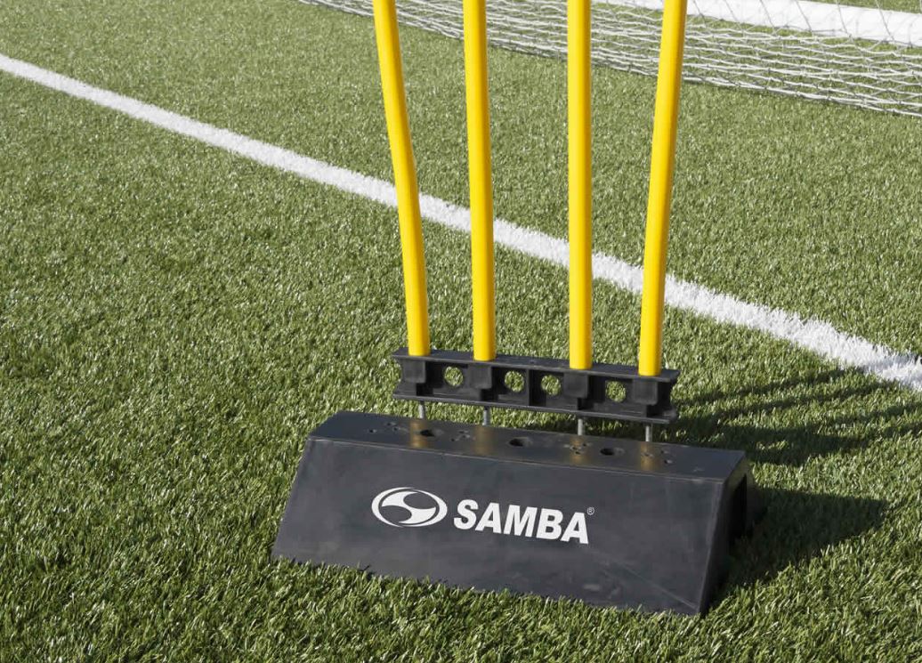 A black and yellow pole on Astro turf is supported by the Samba Sports Samba Rubber Mannequin Base, creating a striking contrast with the green field.