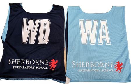 Two Personalised Gilbert Netball Bibs (Single Bibs), one WD in dark blue and one WA in light blue, both featuring Sherborne Preparatory School and a red lion logo printed at the bottom, by Gilbert.