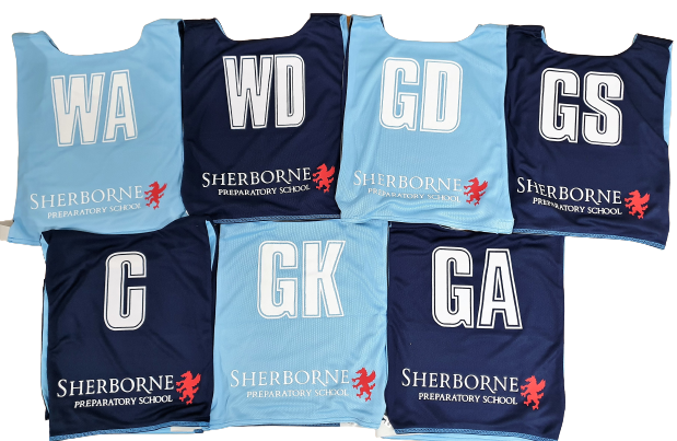 Seven Gilbert Personalised Netball Bibs (Single Bibs) in light blue and navy, each with a unique position (WA, WD, GD, GS, C, GK, GA), Sherborne Preparatory School name and red lion logo on every bib.
