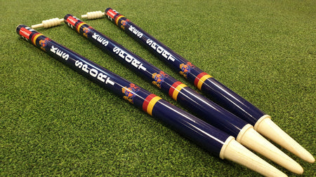 Three Gray Nicolls Custom Printed Club Cricket Stumps, featuring blue color, white tops, colorful stripes, and custom logos and text in white, are arranged parallel on green artificial turf.