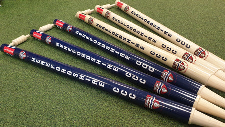 Six Custom Printed Club Cricket Stumps by Gray Nicolls on green turf—three dark blue with white logos, three light beige with matching logos—feature spiral-shaped tops, perfect for personalised cricket matches and club branding.