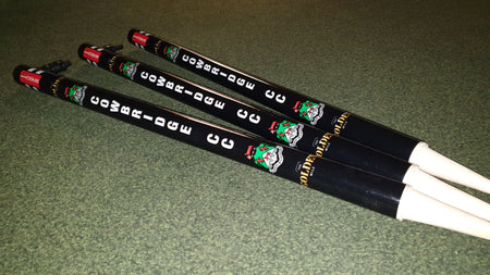 Three Gray Nicolls Custom Printed Club Cricket Stumps, with unique designs for your club, stand side by side—just as practice chanters with white mouthpieces display musical notes on a green carpet.