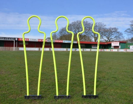 Three Samba Sports Pep Pro Junior Mannequins (set of 3, with carry bag) stand on grass in front of a stadium and trees under a clear sky, perfect for free kick practice.