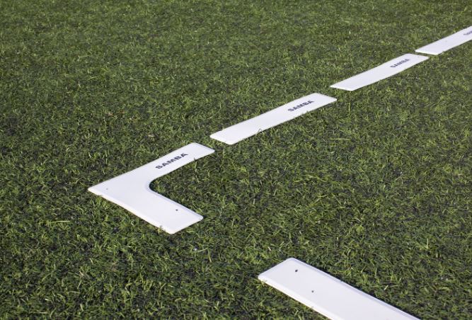 Samba Pitch Marker Set by Samba Sports features white L-shaped and rectangular rubber markers labeled BASE A, arranged on green artificial turf, ideal for setting up sports drills or coaching areas.