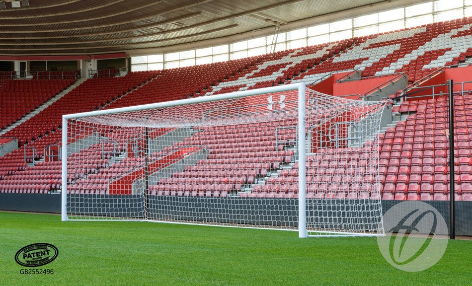 A Harrod Sport 4G Stadium Pro Goal made from aluminium stands on a green field in an empty stadium with red seats. The stands display a white pattern, and logos are visible on the image. The goal is equipped with a reinforced net support system for enhanced durability.