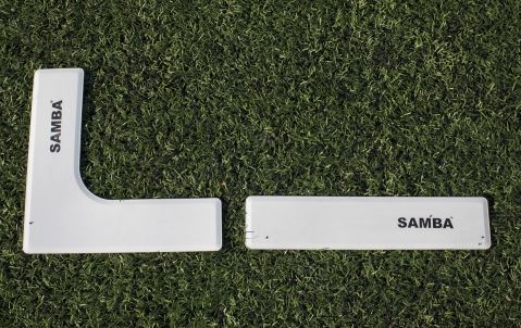 The Samba Pitch Marker Set by Samba Sports includes two white plastic markers—one L-shaped and one rectangular—positioned on artificial grass, ideal for marking coaching areas on the field.