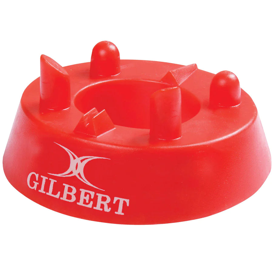 The Gilbert 320 Precision Kicking Tee is a red moulded rubber tee from Gilbert, featuring four raised prongs and a white Gilbert logo on the side, designed for accurate rugby kicking.